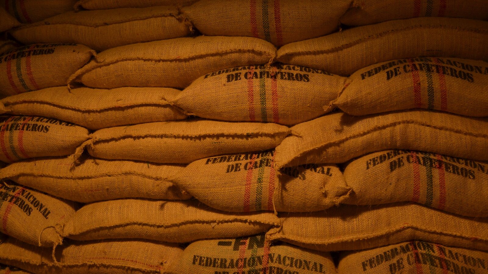 Sacks of green coffee stacked in rows in a warehouse.