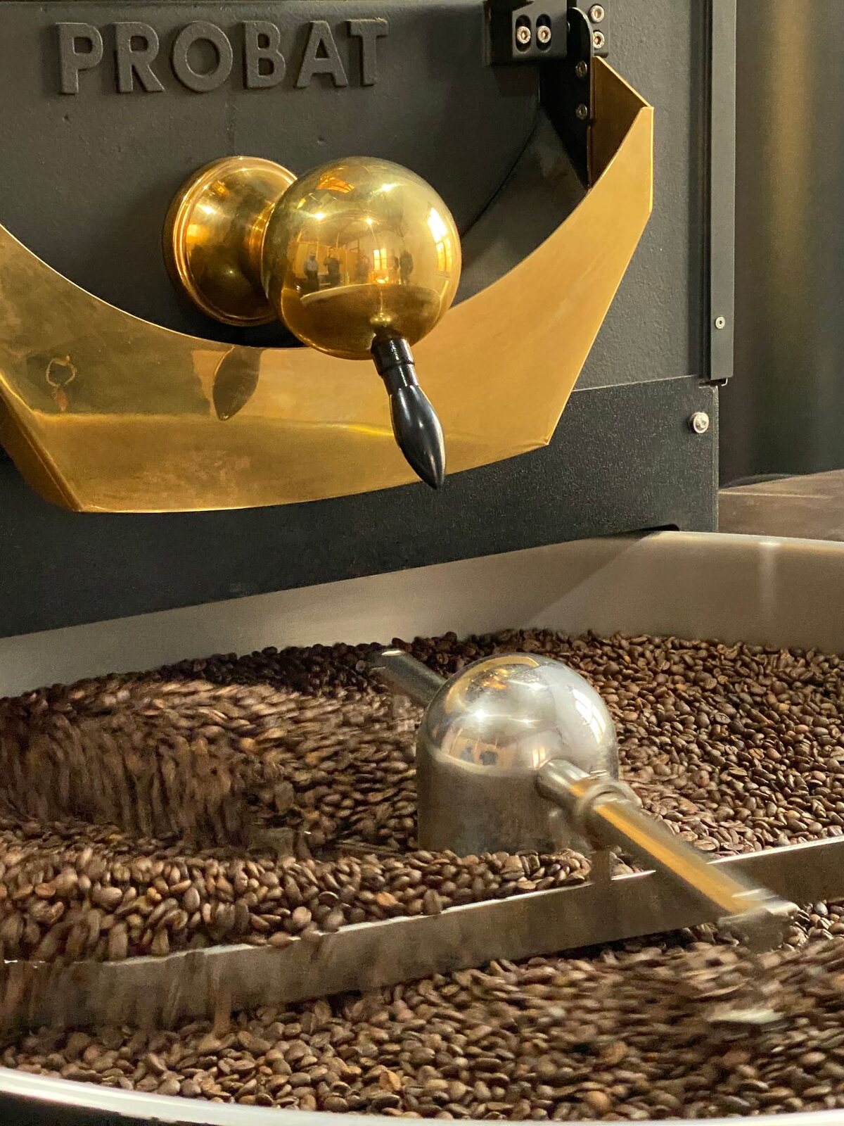 Beans turning inside the drum of a shop roaster, seen through the open hopper.