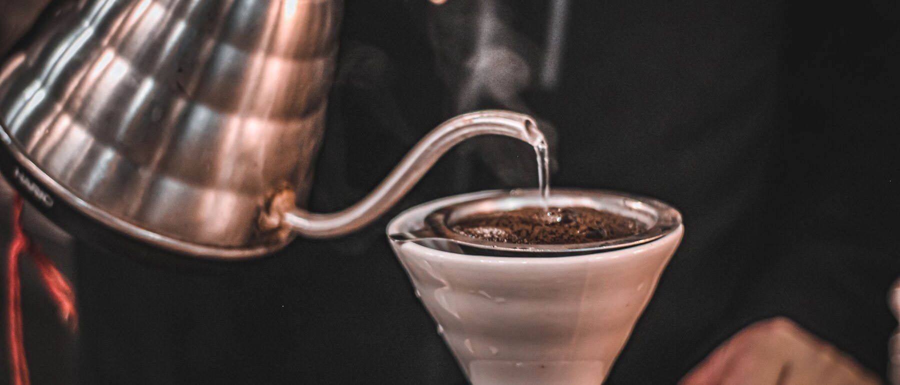 Water poured from a gooseneck kettle onto ground coffee in a ceramic dripper.